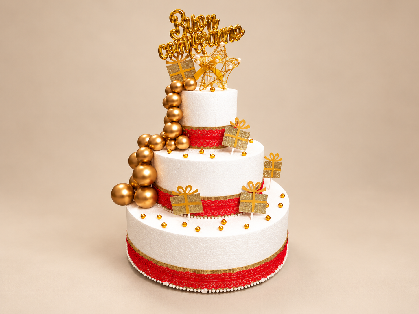 Composizione in polistirolo bianco con scritta Buon compleanno, decorazioni oro e rosse su fondo champagne